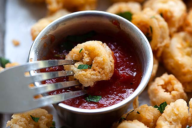 A piece of fried calamari dipped into fried calamari sauce.