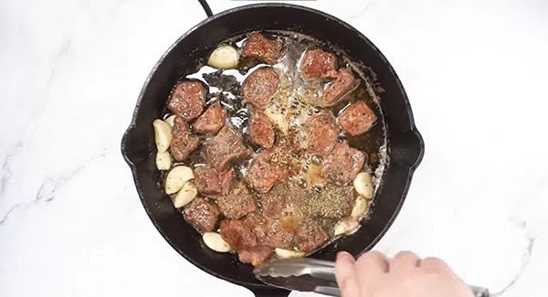 Add Italian seasoning and dry rub into the cast iron with the steak bites and garlic. 