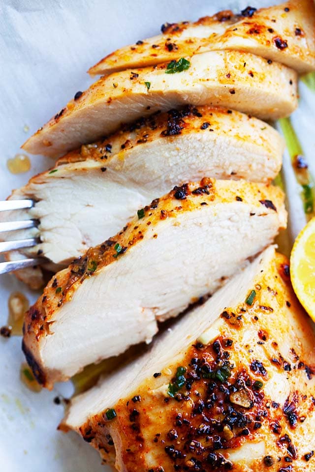 Sliced boneless chicken breast with lemon wedges.