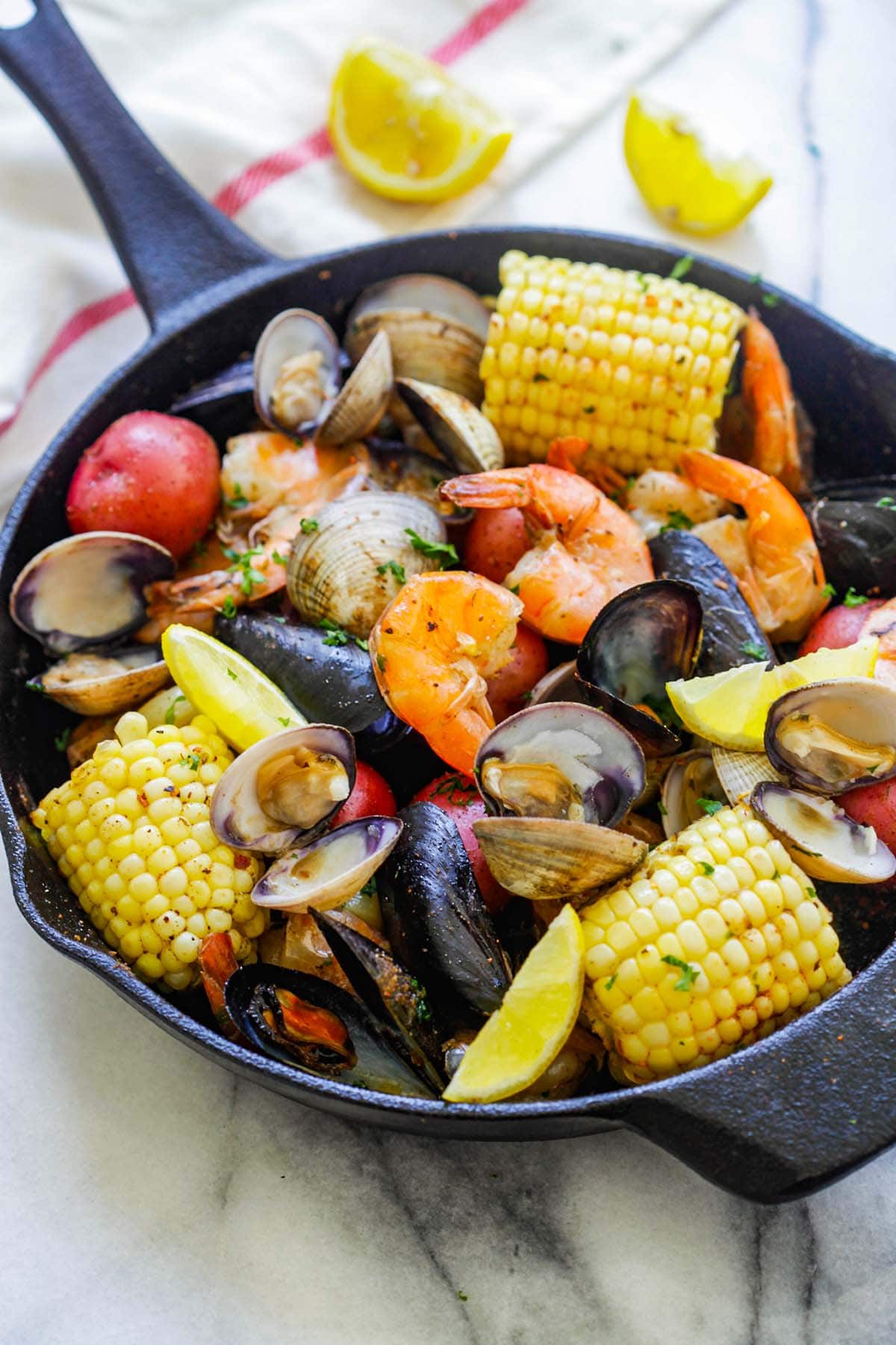 Scenic view of a delectable and easy clambake, featuring an assortment of seafood of with clams, mussels, shrimp, corn and potatoes.