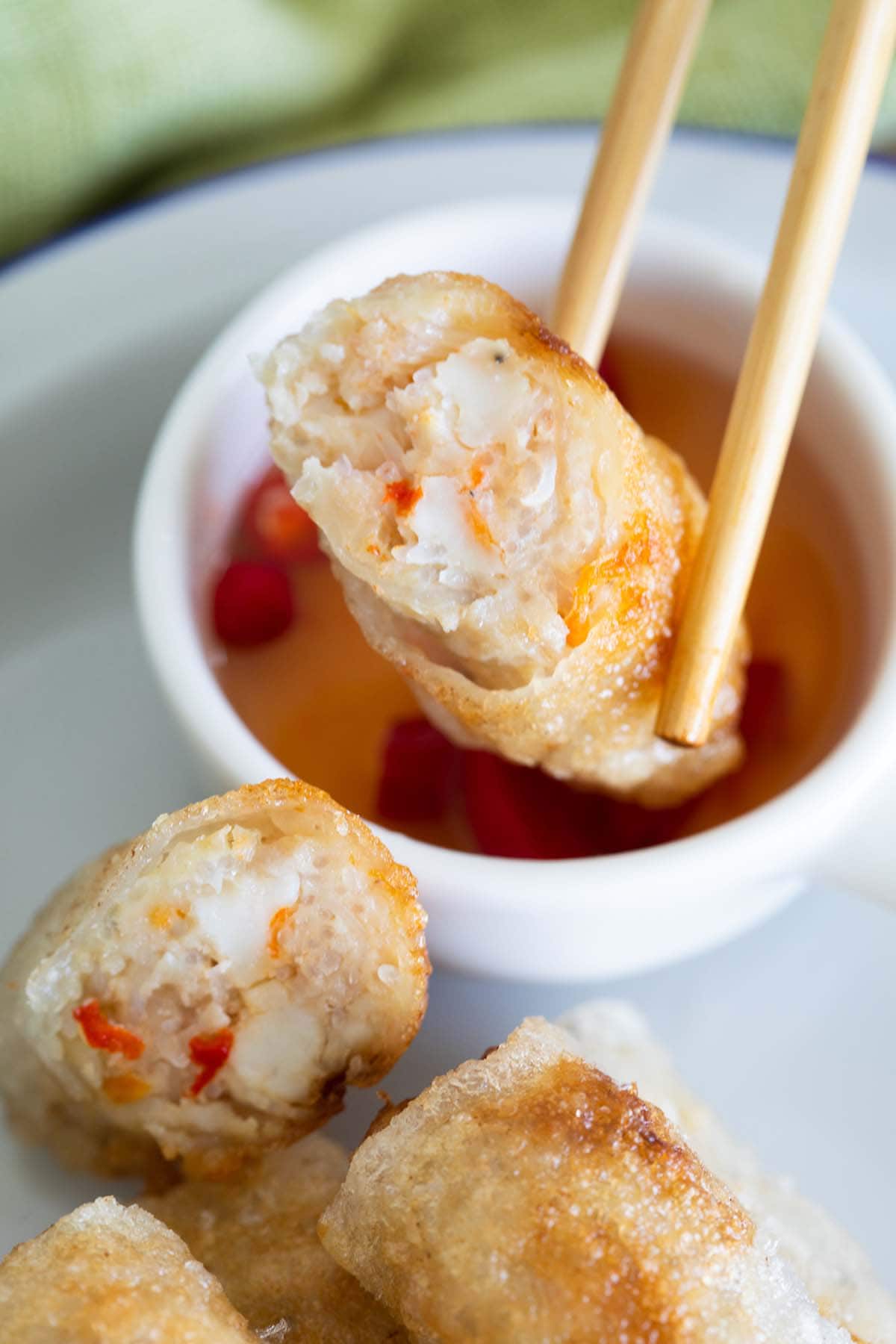 Vietnamese spring rolls held by a chopstick dipping into the sauce. 