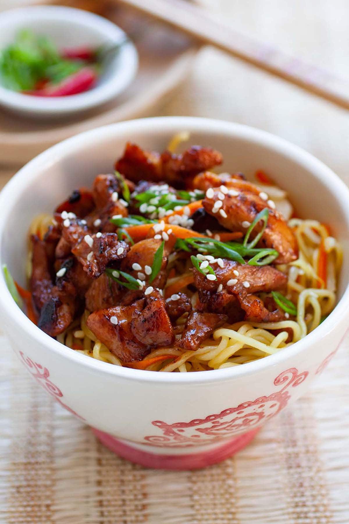 Chicken stir-fried noodles complete with carrots and green onions in a bowl.