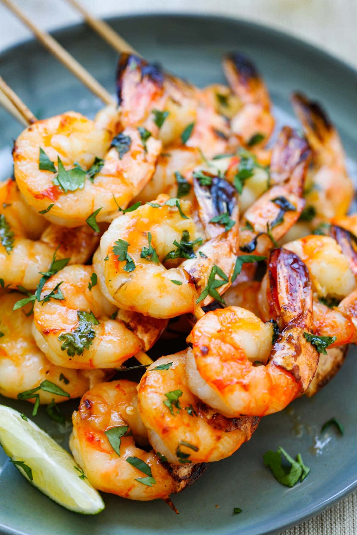 Shrimp skewers coated with honey Sriracha butter with lime wedges served on the side on a plate.