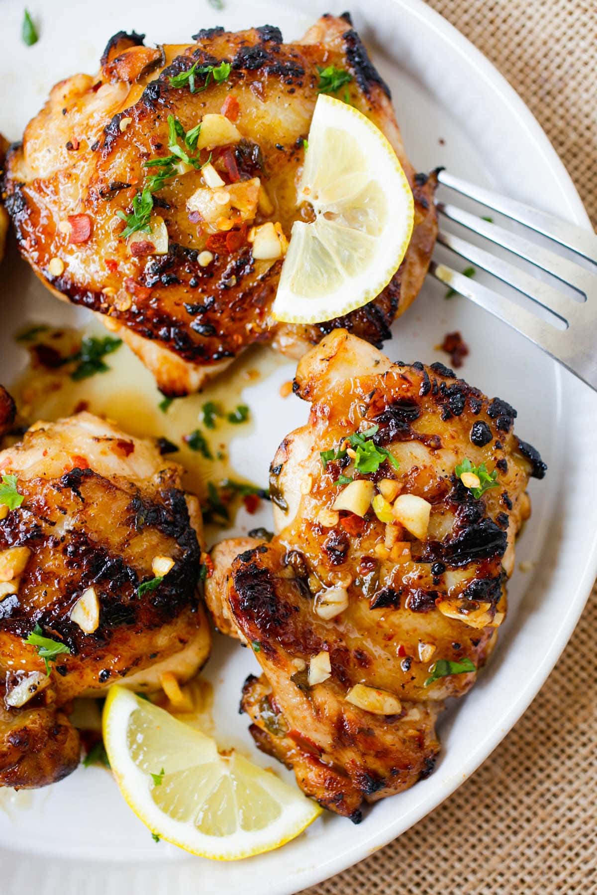 Grilled chicken thighs covered in citrusy lemon and savory garlic sauce served on a plate.