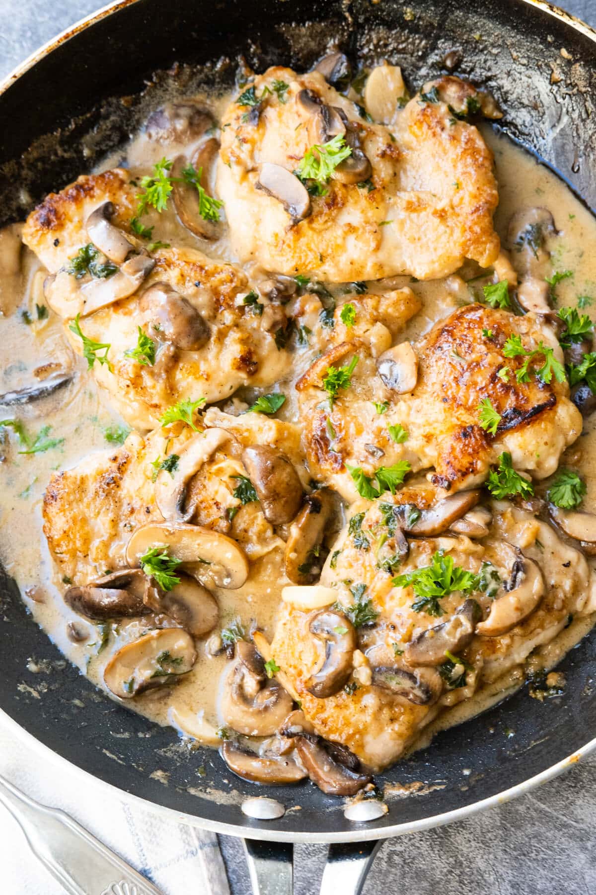 Chicken marsala bathed in rich marsala wine sauce in a skillet.