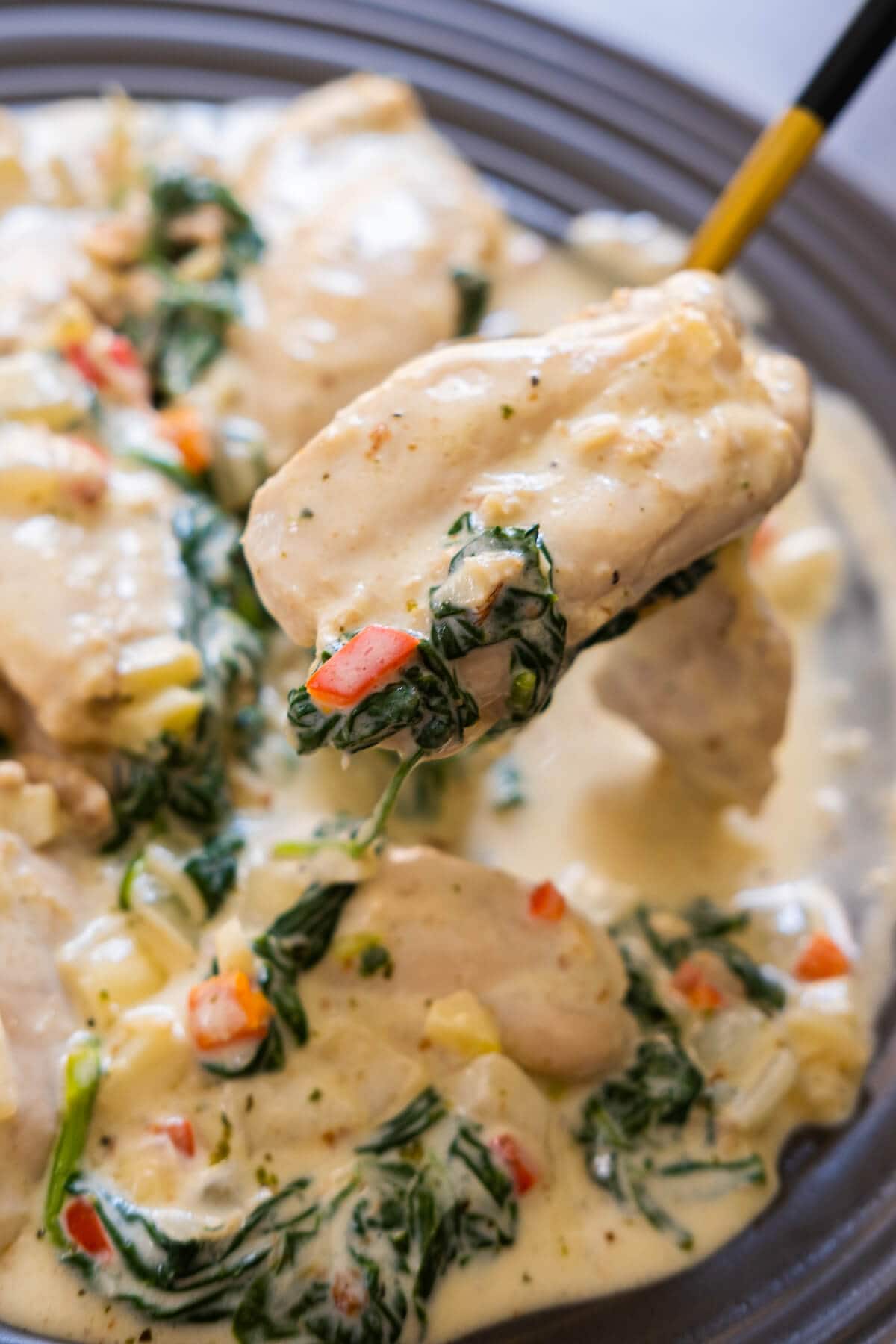 A spoon of perfectly seared chicken thighs in creamy Parmesan sauce with spinach leaves. 