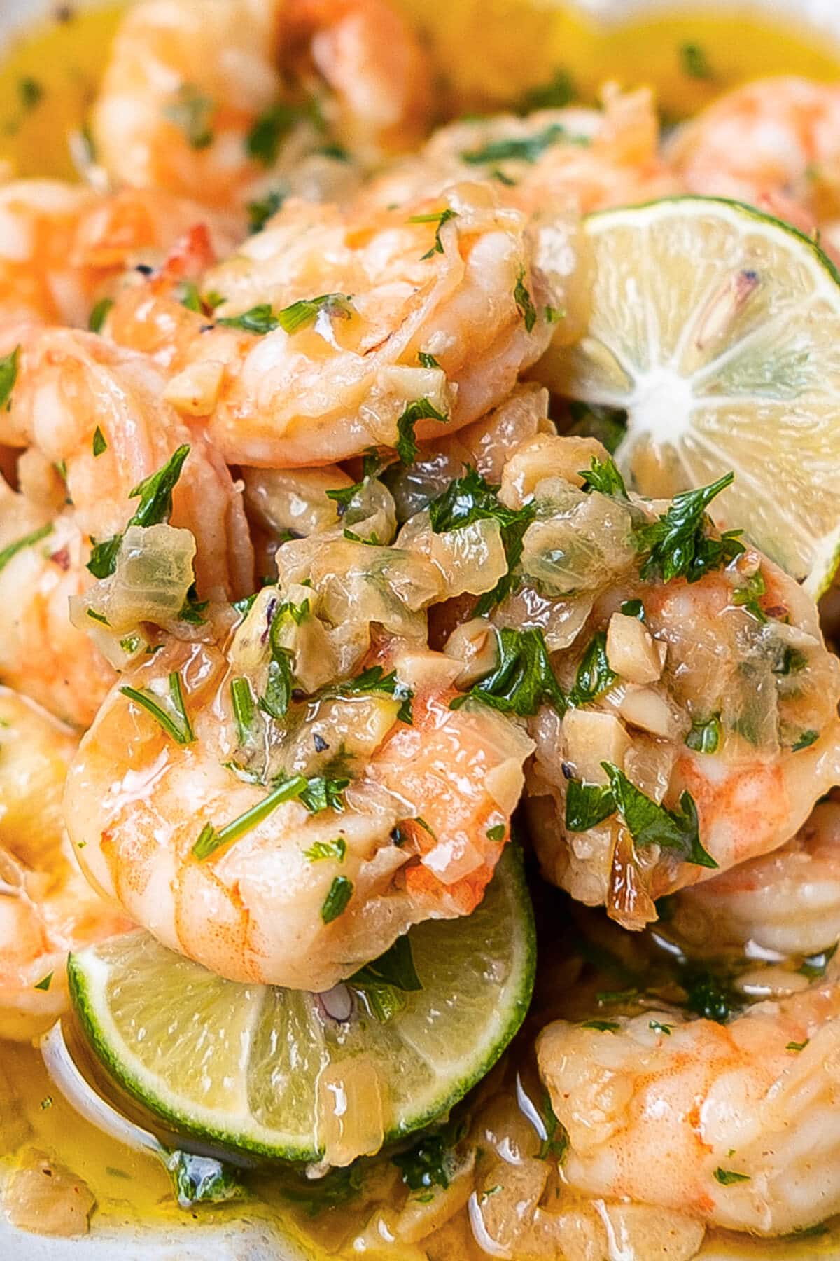 A close up shot of plump and succulent shrimp immersed in a delectable garlic and white wine sauce with lime slices. 