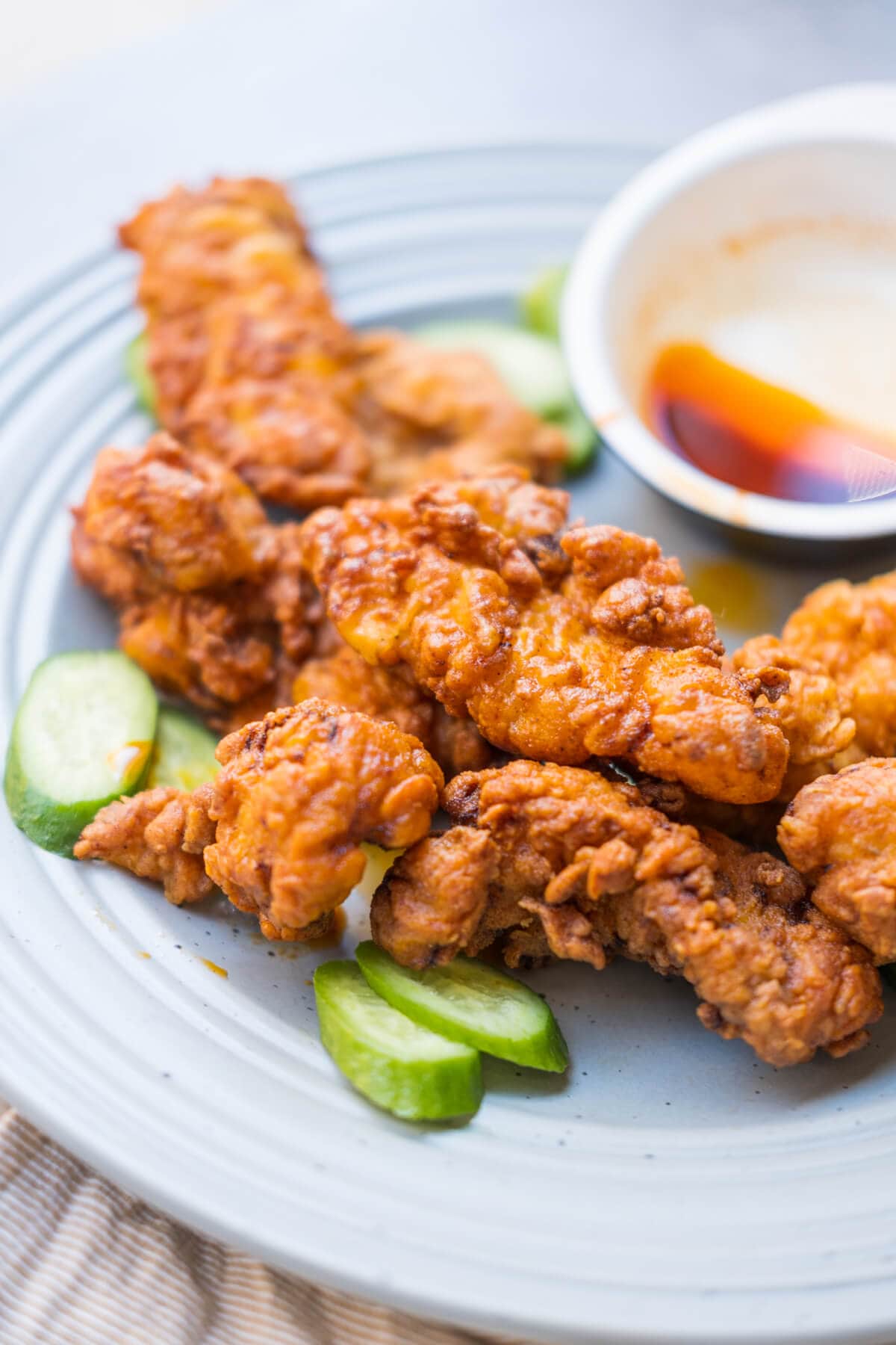 Fried chicken tenders marinated with various spices served with cucumbers on a plate.