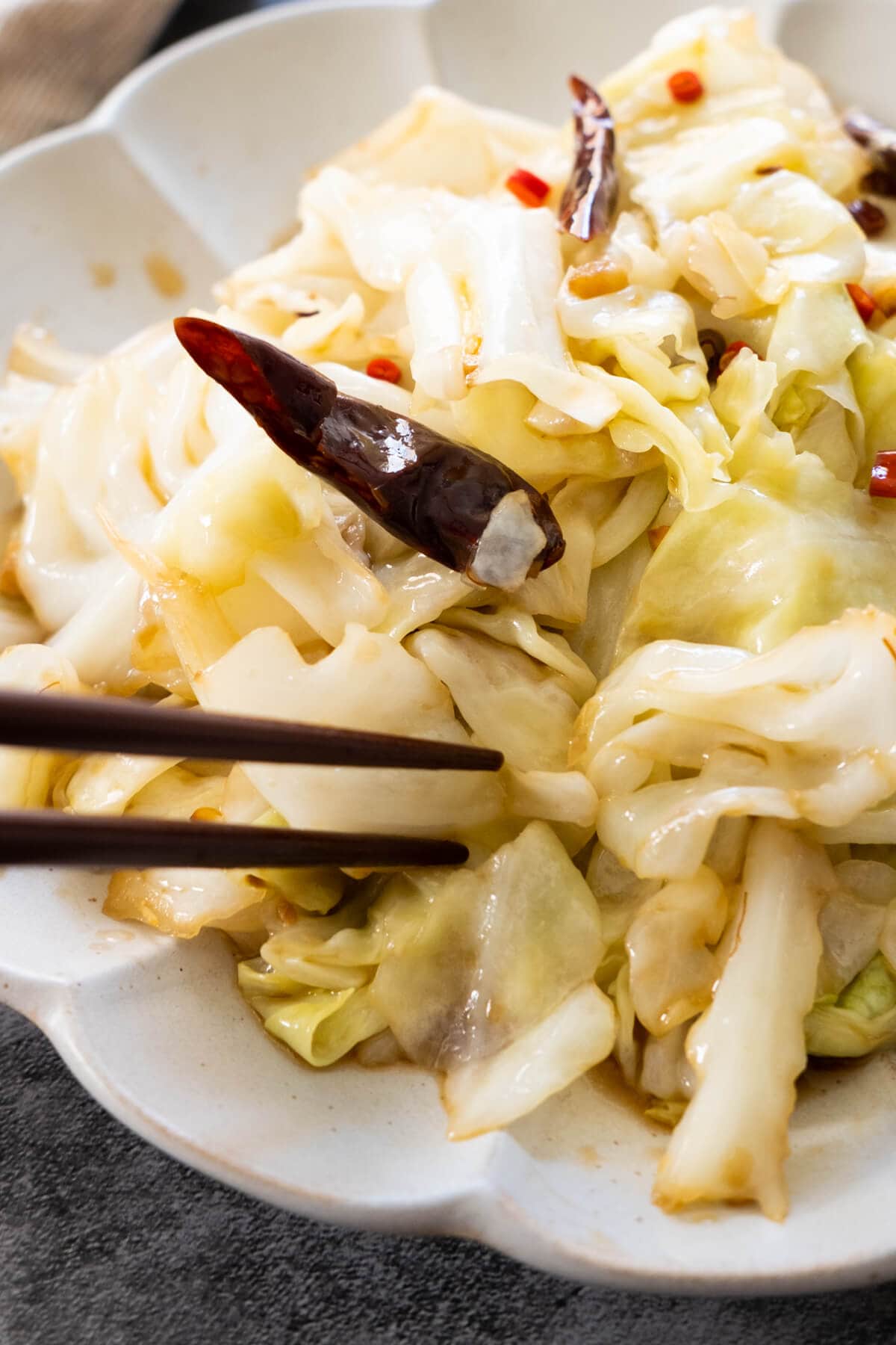 A chopstick picking up a piece of cabbage that is cooked with dried chili. 