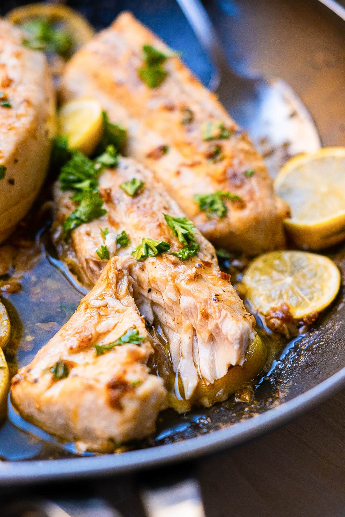 Mahi-mahi fillet being cut half opened revealing its pink inside bathed in a rich and savory garlic butter sauce in a plate. 