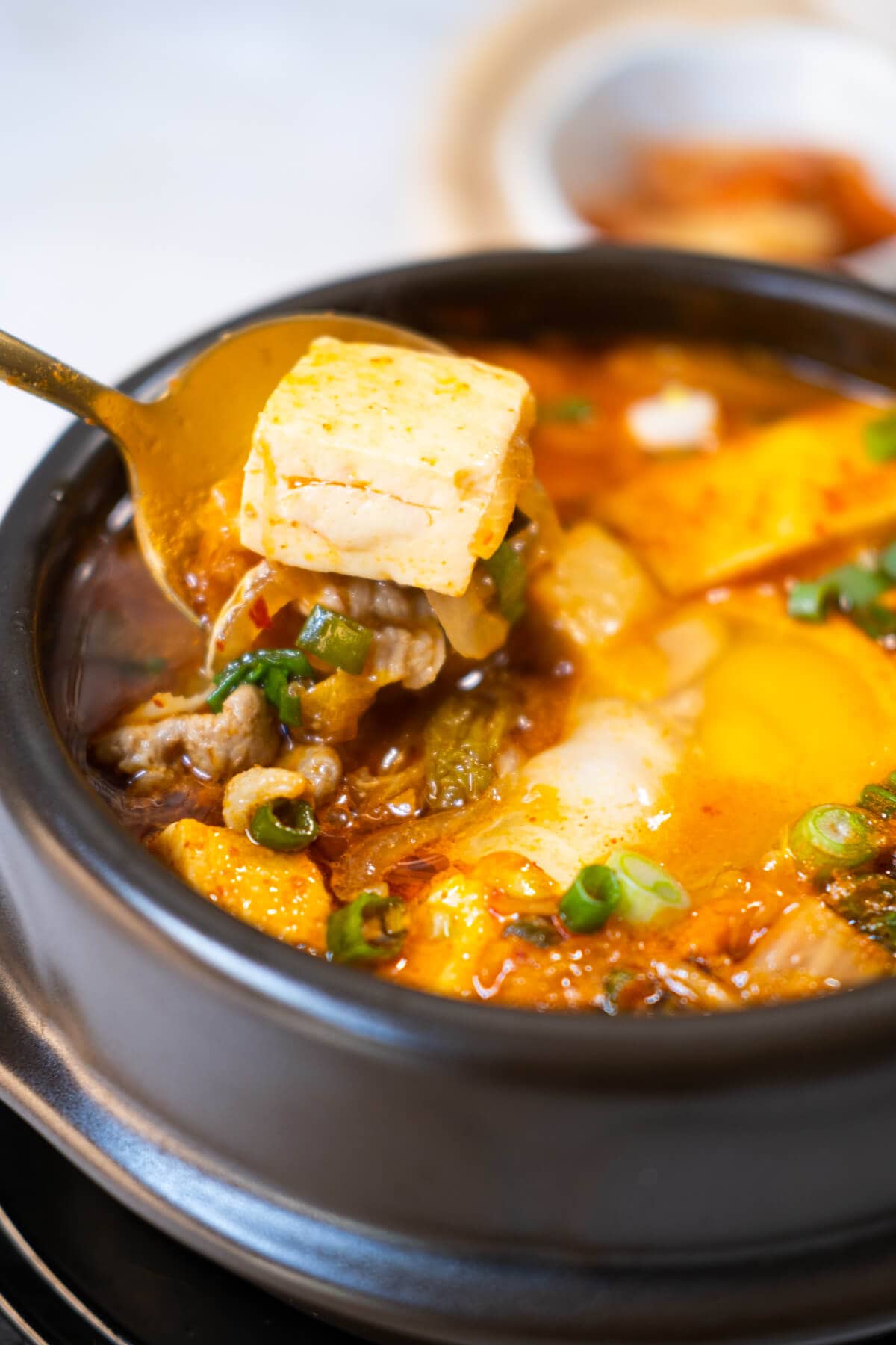 A spoon scooping a tofu out from the stew. 