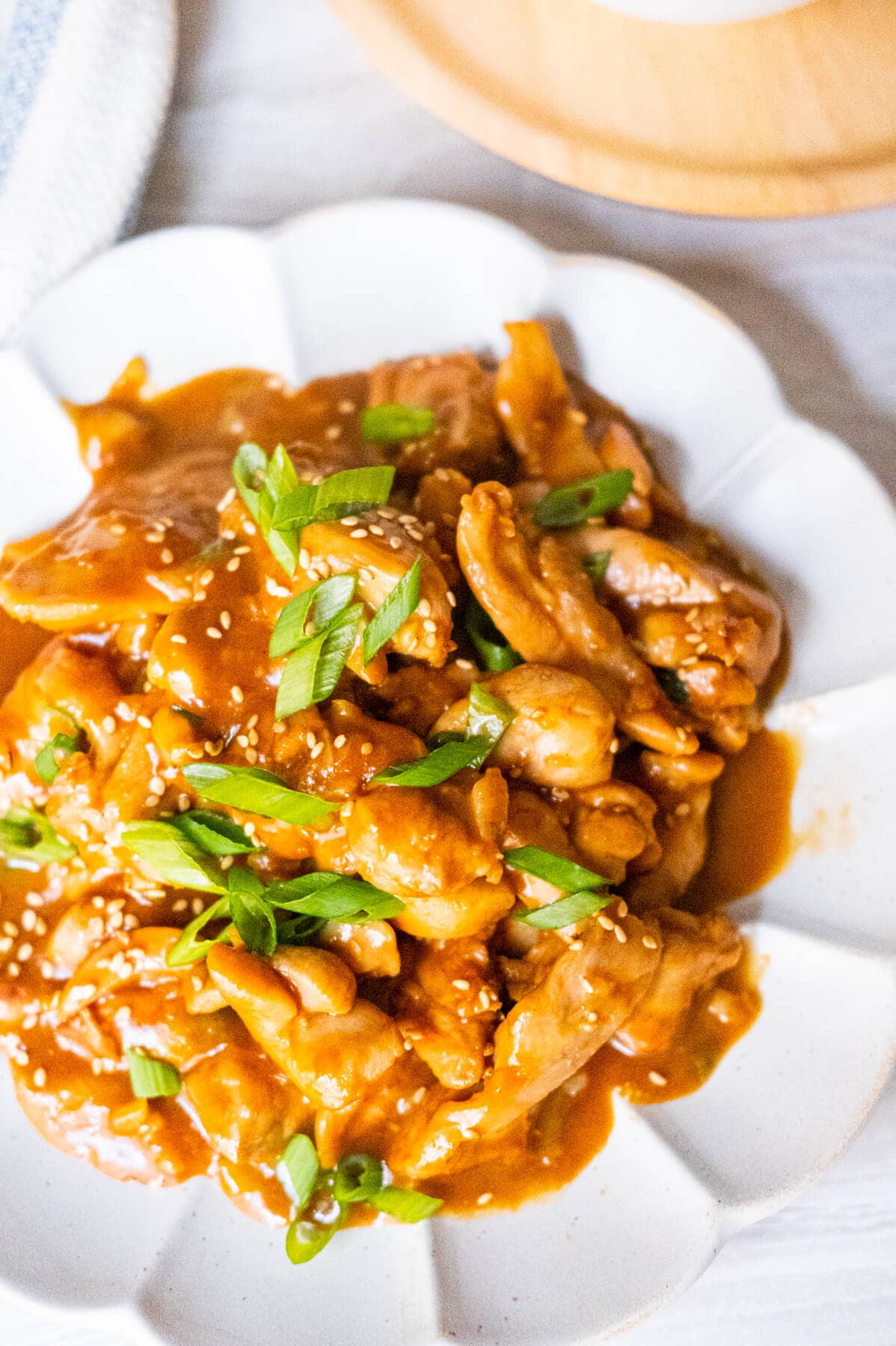 A plate of rich and sweet Bourbon chicken sprinkled with white sesame and scallions served in a white plate. 