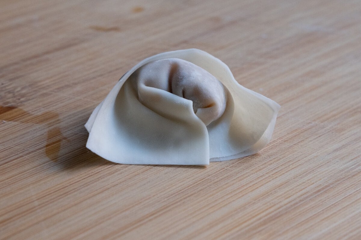 Raw chicken wonton sitting on top of a board.