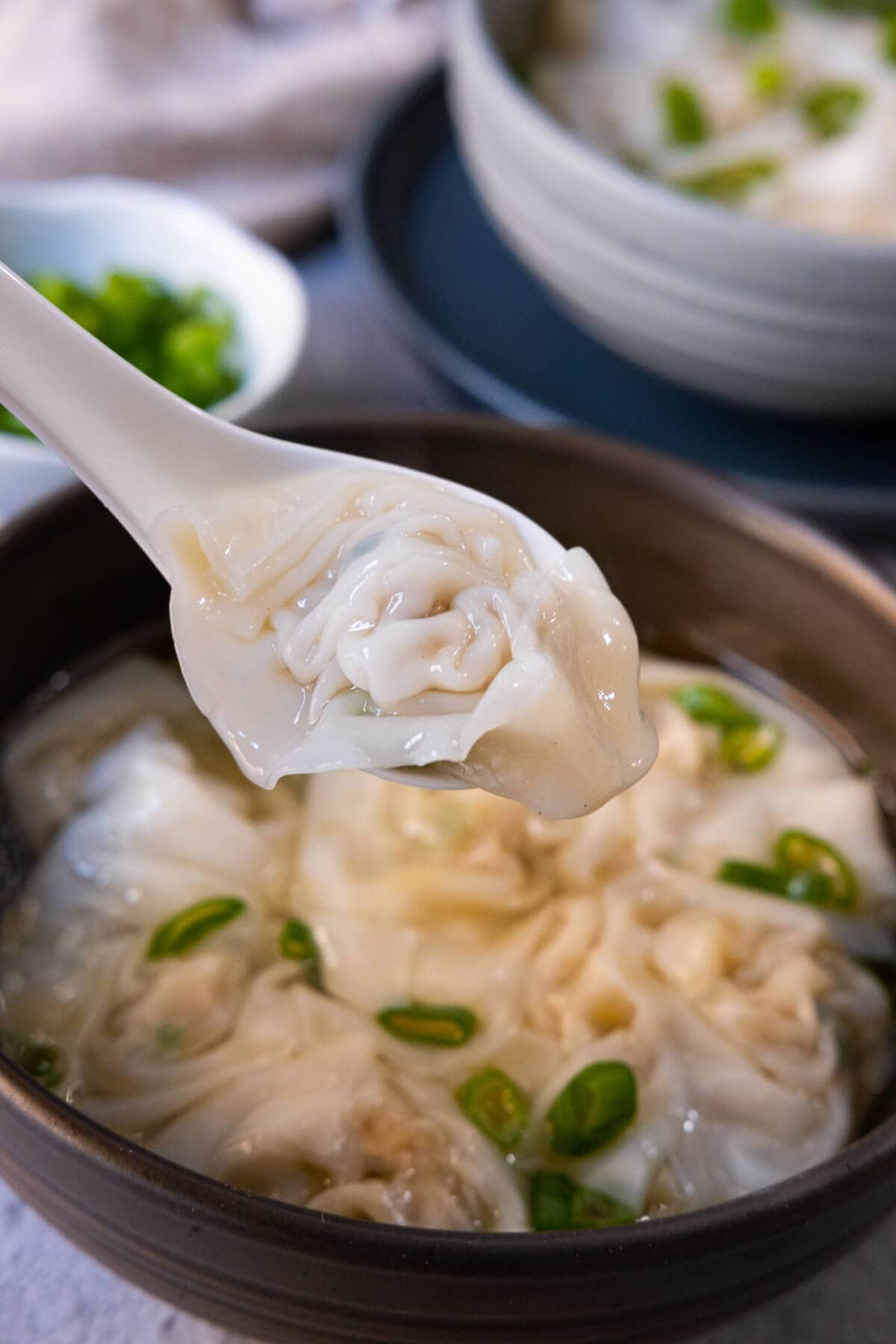 A Chinese soup spoon scooping up a chicken wonton in soup.