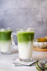 Two iced Matcha latte with a small plate in the back.