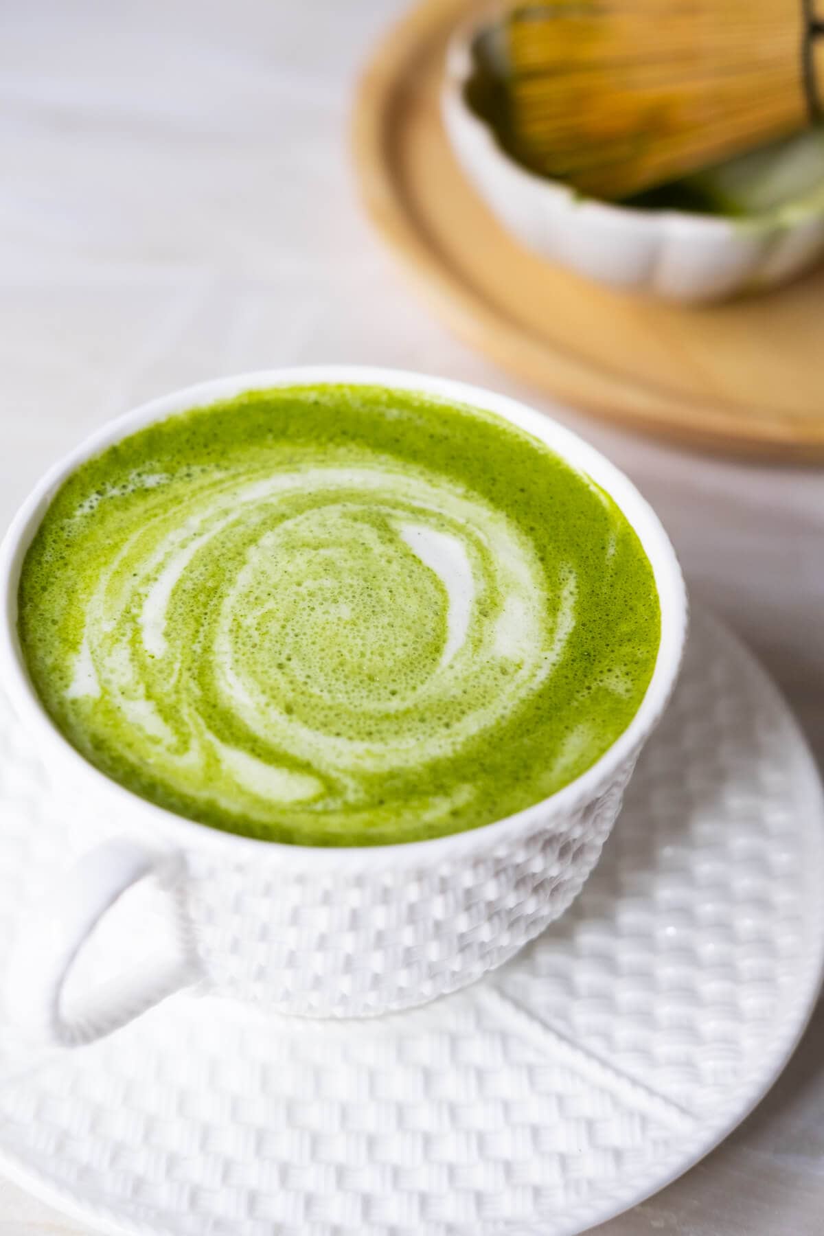 Hot matcha latte in a cup with foams on the surface.