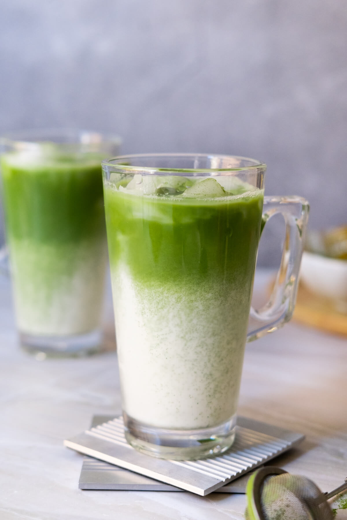 Two glasses of matcha latte on a table.