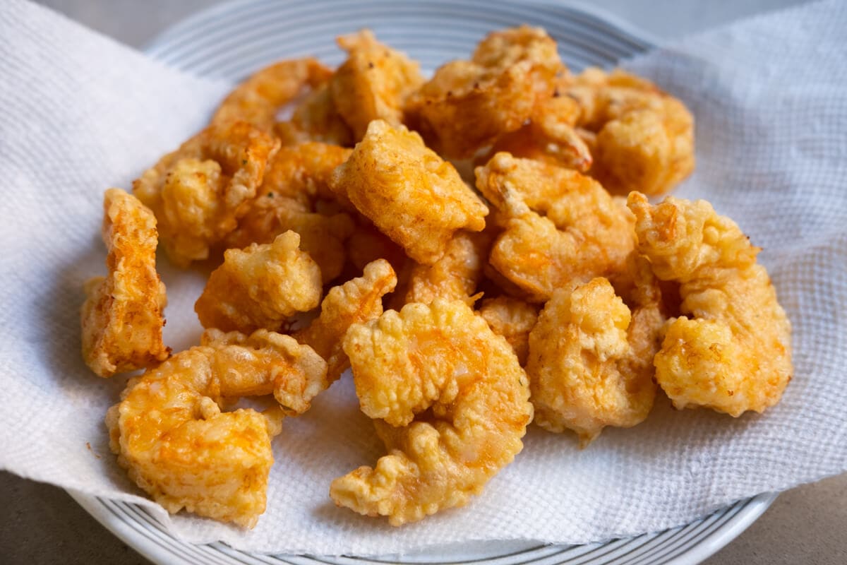 A paper towel lined plate with fried shrimp on it.