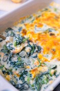 Creamed spinach in a baking dish scooped by a spoon.