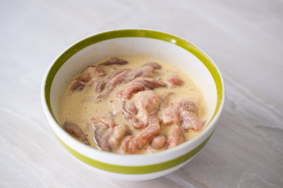 Pork shoulder strips marinating in a bowl. 