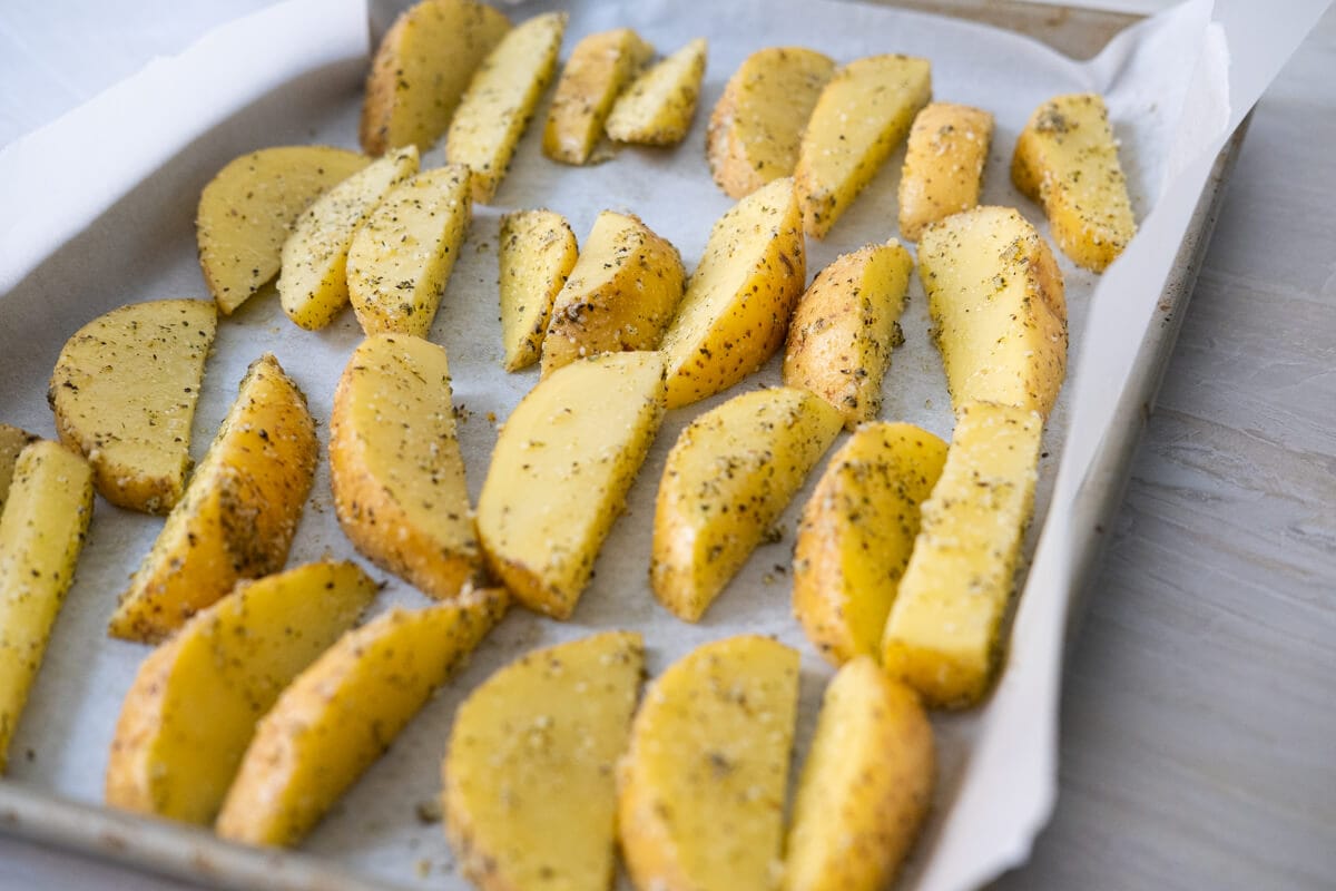 Seasoned potato wedges placed on a baking tray lined with parchment paper in a single layer. 