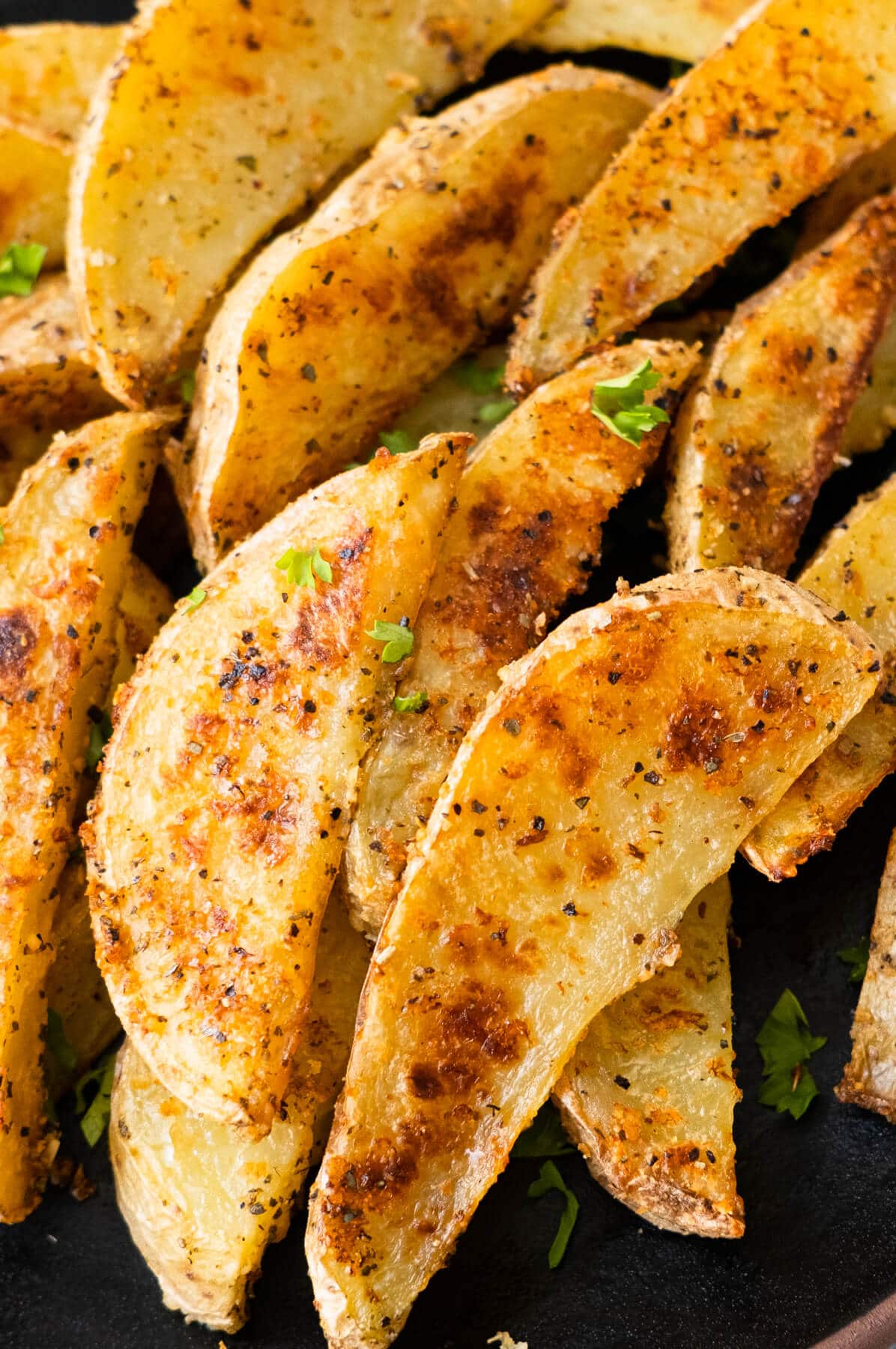 Golden crispy potato wedges with chopped parsley on top.