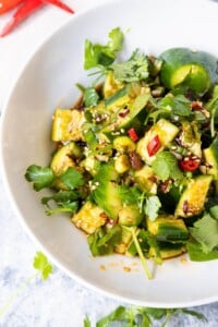 A bowl of smashed cucumber salad with sesame seeds, chopped red pepper and cilantro sprinkled on top.