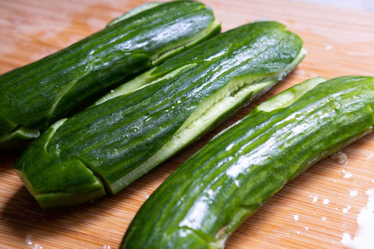 Persian cucumber being smashed until it splits on a cutting board with a knife. 