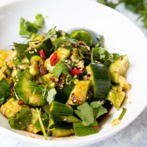 Smashed cucumber salad topped with sesame seeds, red pepper and chopped cilantro.