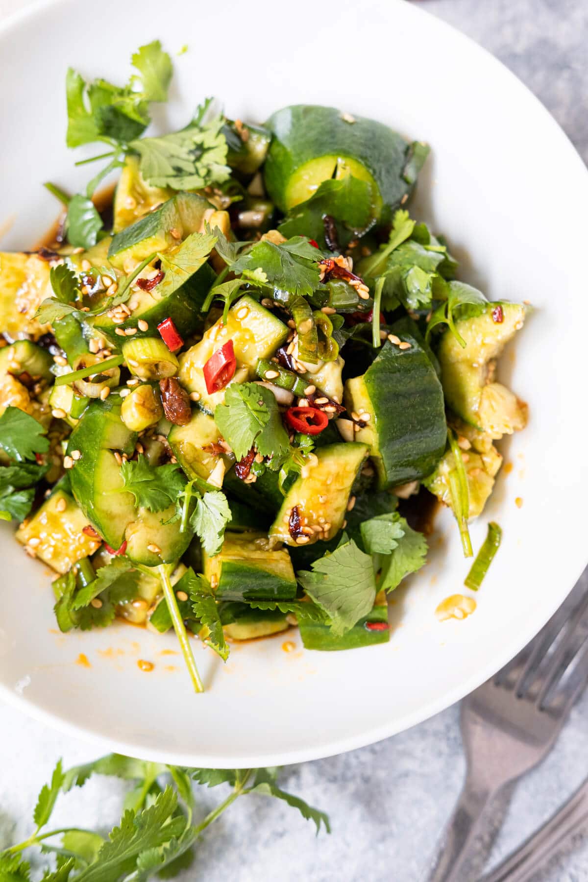 A bowl of spicy smashed cucumber salad with fork and knife placed aside. 