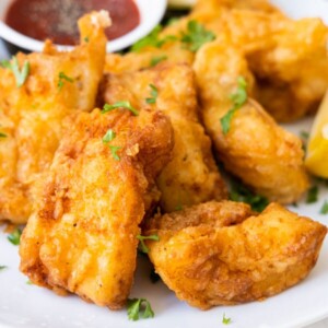 Deep-fried golden crispy beer-battered fish served with ketchup and sprinkled with chopped parsley on top.