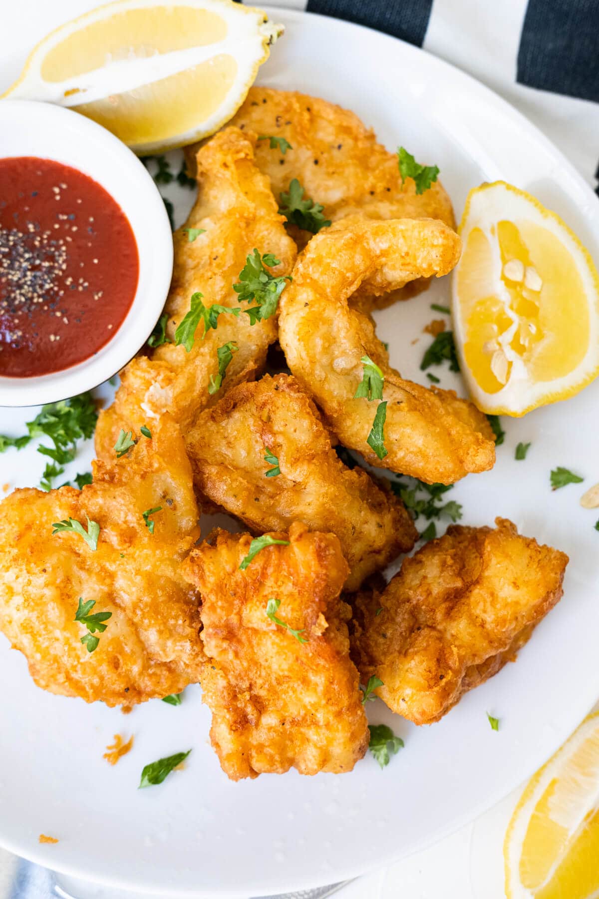 Golden crispy beer-battered fish with lemon wedges and ketchup aside. 