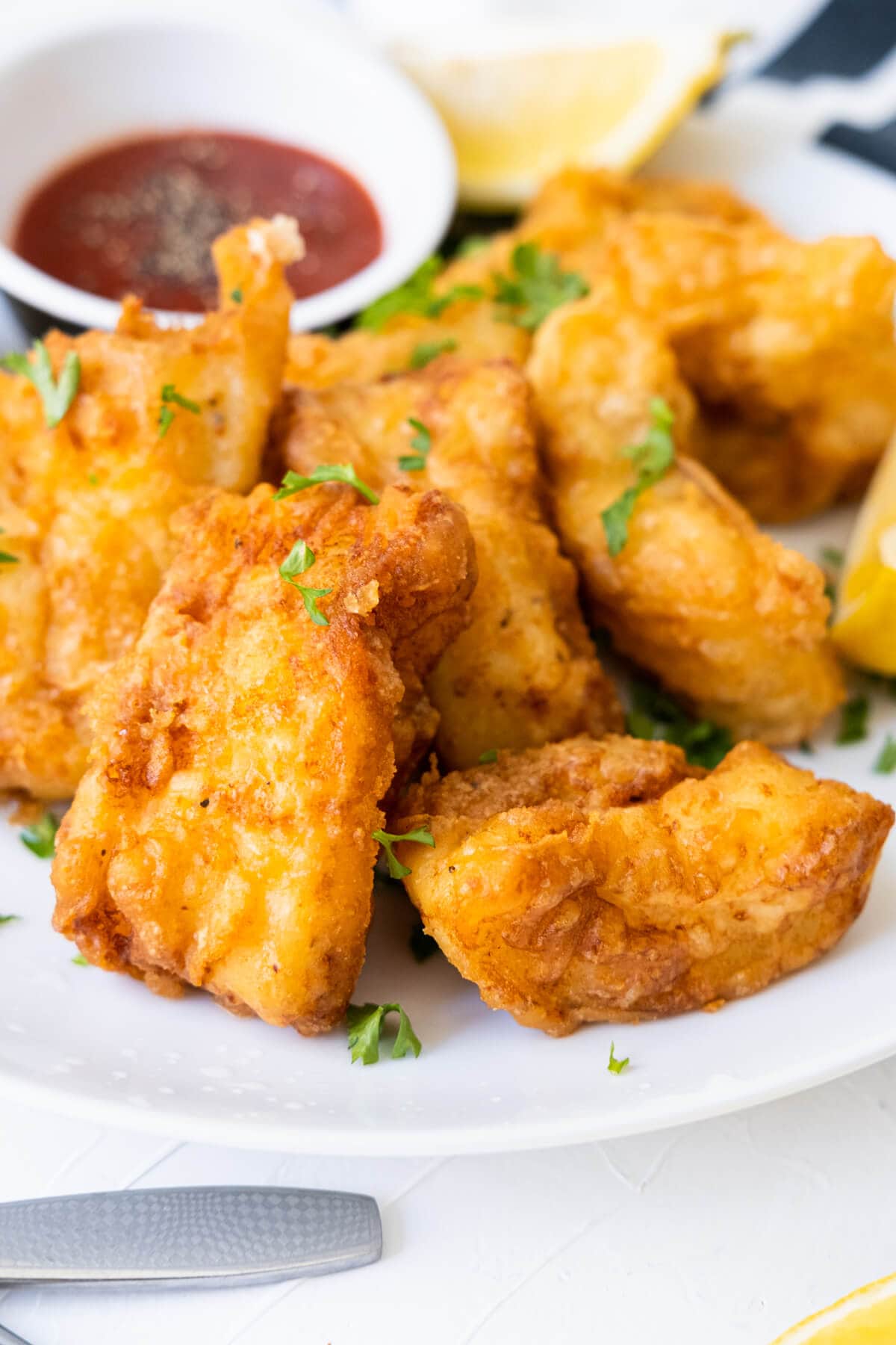 Pieces of fried battered fish on a plate with ketchup and lemon wedges. 