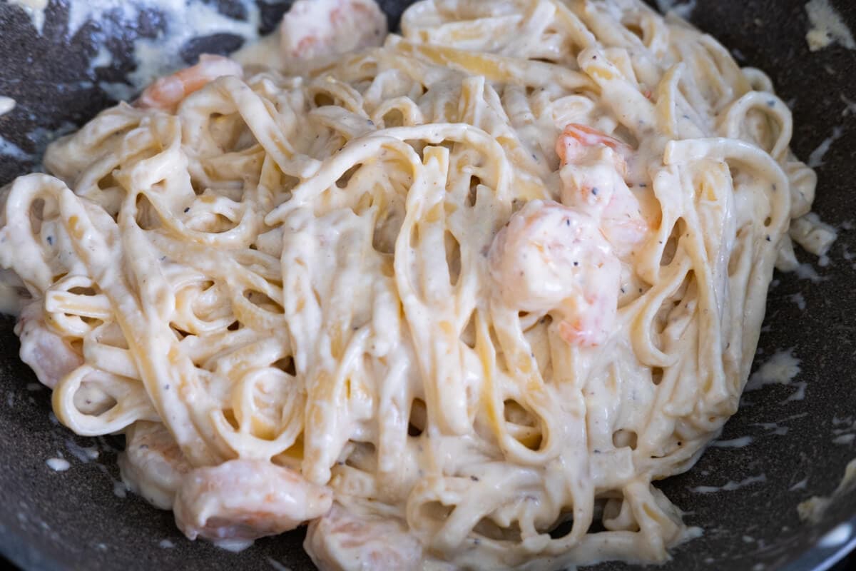 Cooked fettuccine and shrimp to creamy sauce stirred and combines in a pan. 