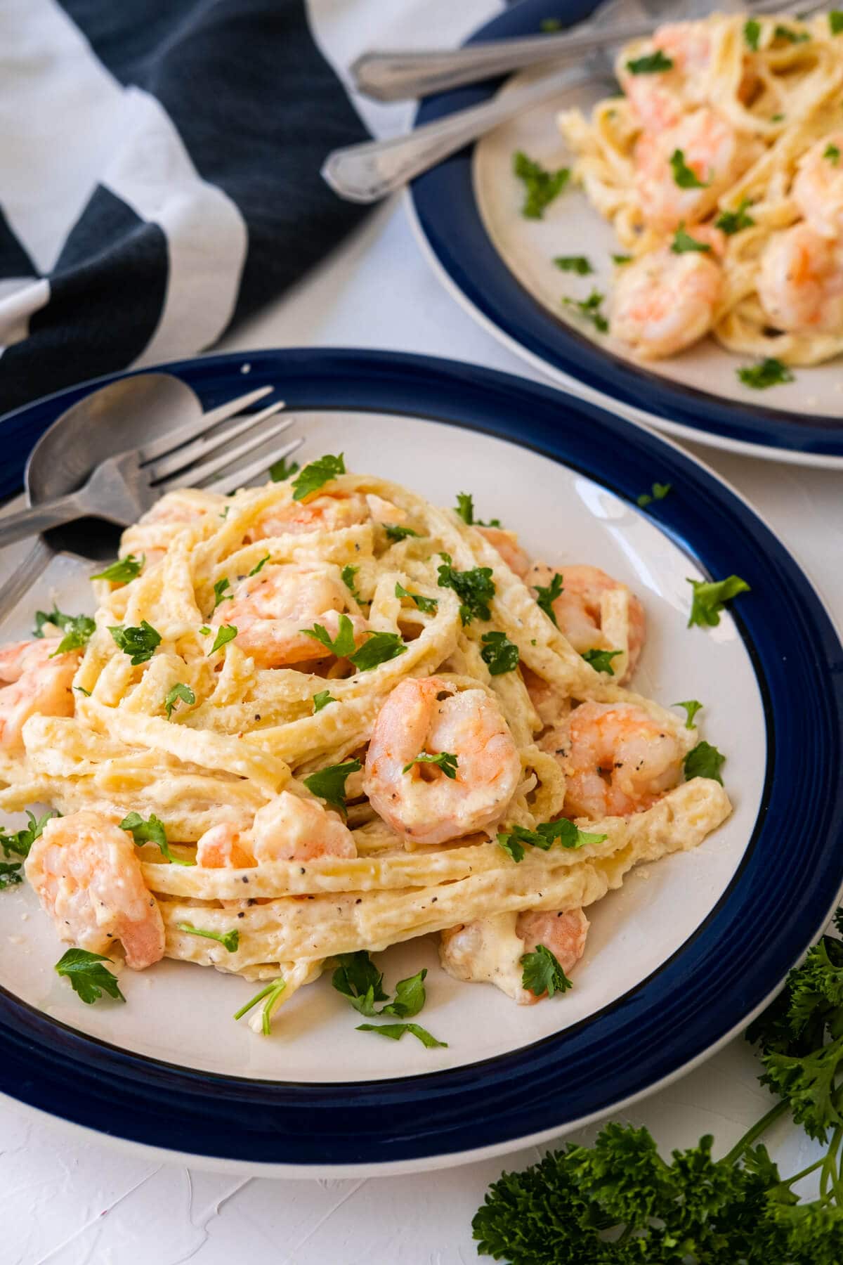 Rich, creamy fettuccine Alfredo served with shrimps on the plate with a white and navy color kitchen towel placed aside.