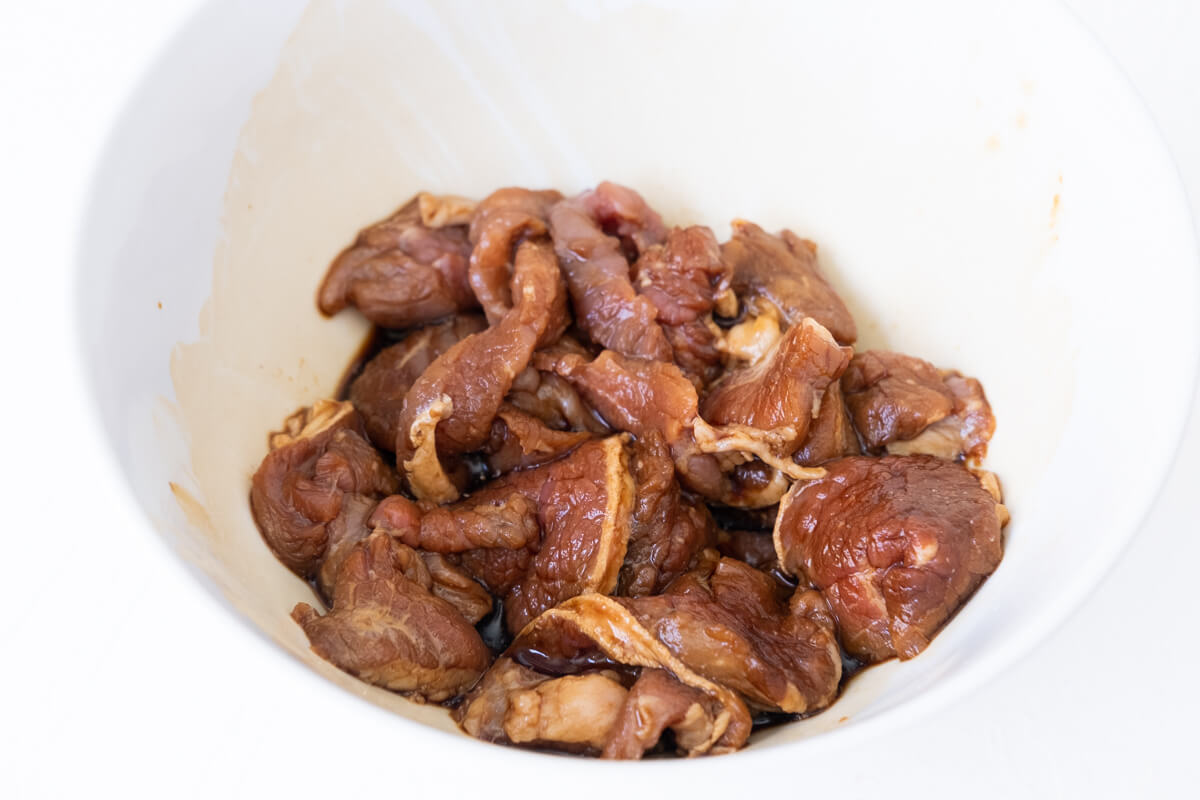 Beef slices marinated in soy sauce, dark soy sauce, Chinese rice wine, and cornstarch in a bowl. 