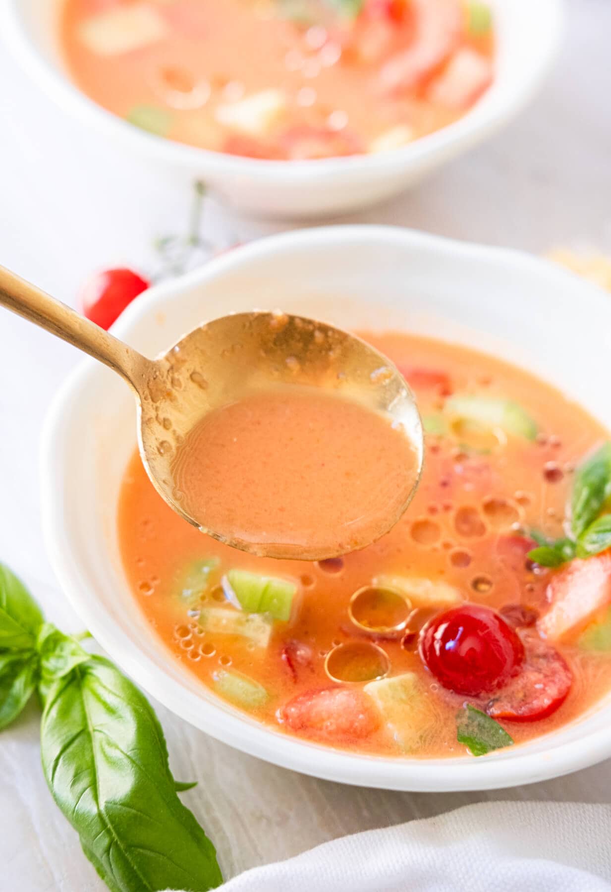 A spoon scooping out one scoop of  the gazpacho soup from a bowl. 