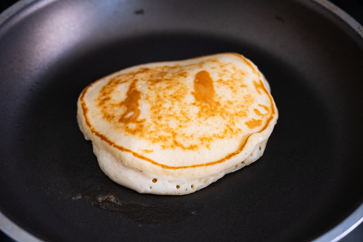 Batter cooked with its bottom part is golden and bubbles appear on the edges on a nonstick frying pan. 