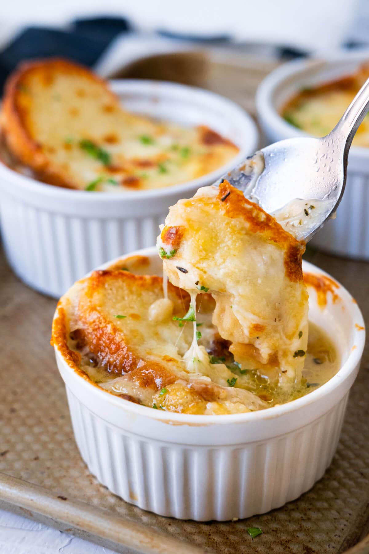 A spoon scooping off a spoonful of French onion soup scoop up with melty cheese and soggy bread. 