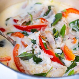 Spicy coconut chicken stew with red bell pepper, baby spinach leaves and fresh basil leaves on top.