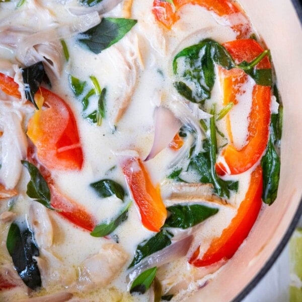 Spicy coconut chicken stew with spinach leaves and basil leaves on top.