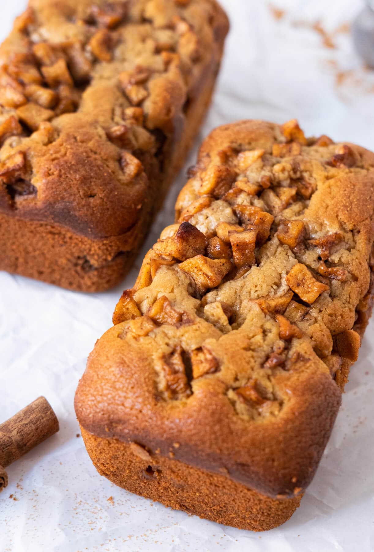 Two small loaves of bread with crisp apple bites on top and in between with one loaf having two slices of it cut off from the loaf. 