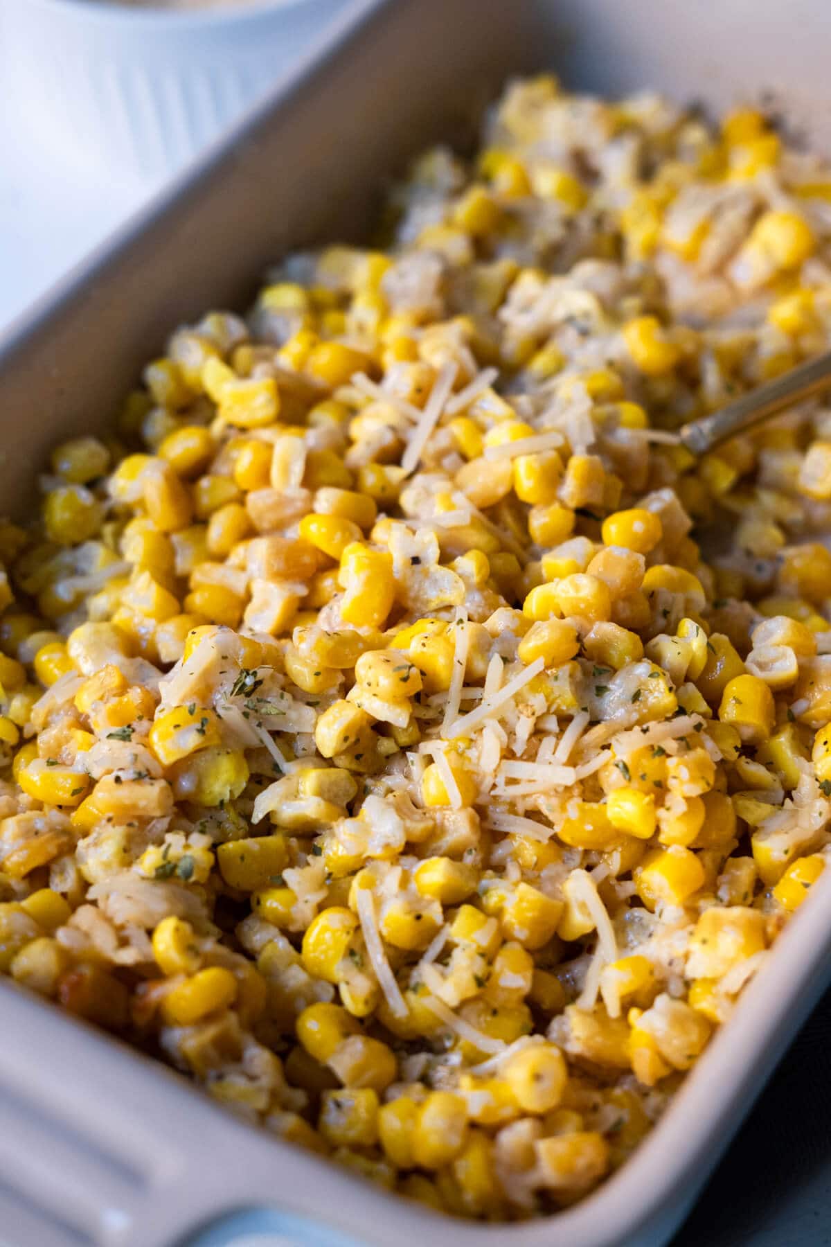 Baked corn in a baking dish with shredded parmesan and parsley flakes on top. 