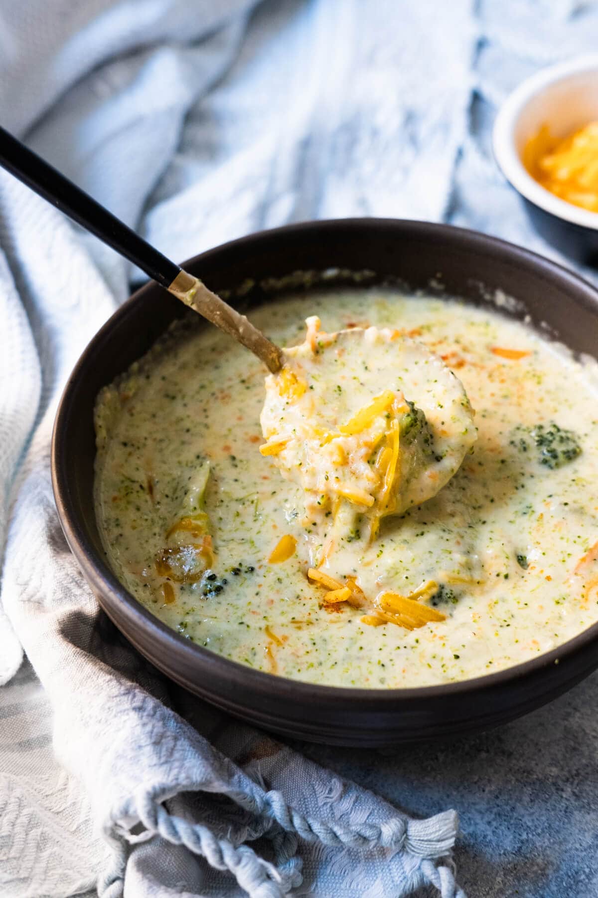 Soup with broccoli and cheddar inside served in a small plate of extra cheddar cheese on the side. 