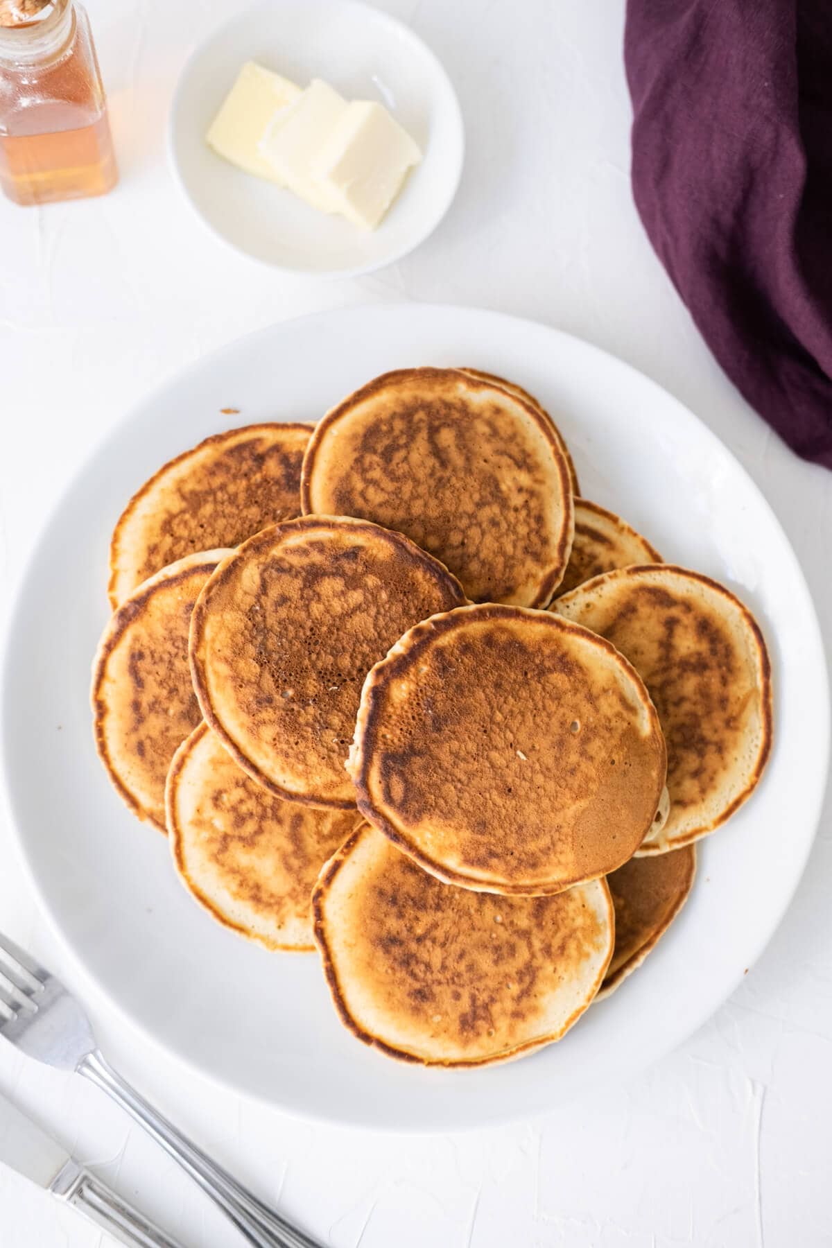 Queen Elizabeth II's drop scones stacked on a plate with butter and syrup aside. 