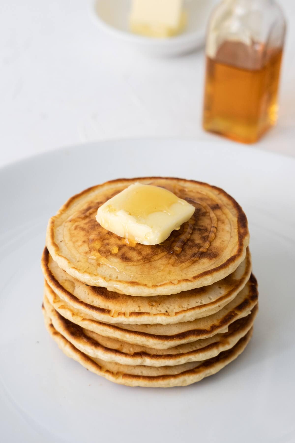 Scones stack tall with butter on the top on a white plate. 