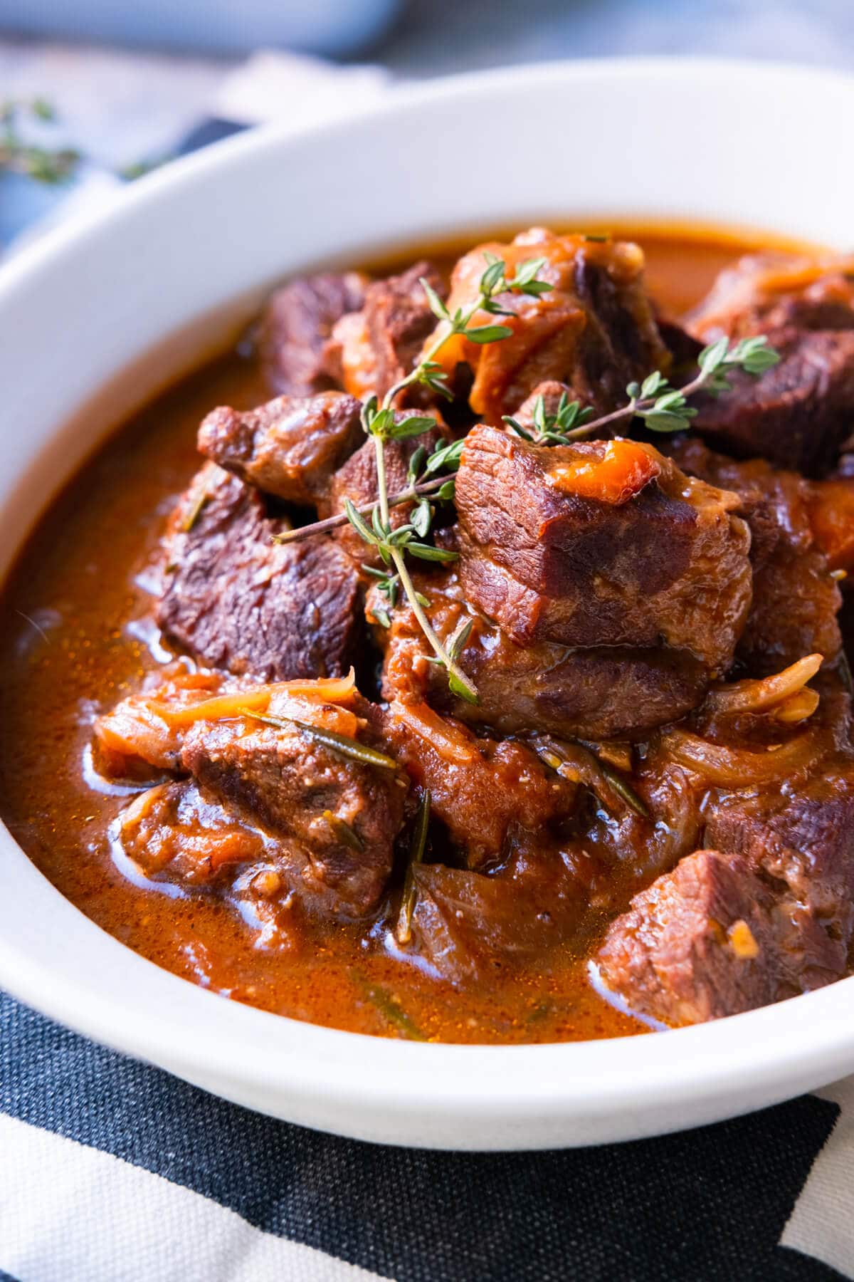 Homemade beef soaked in red wine sauce in a bowl topped with fresh thyme.