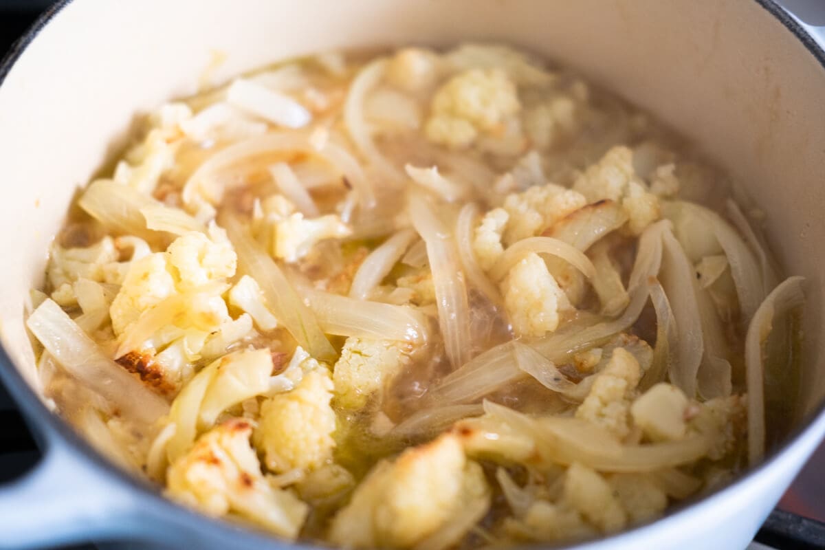 Cauliflower florets and onion simmering in a heavy-bottom pot. 