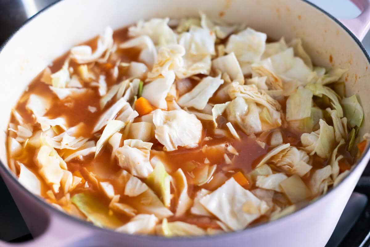 Beef broth and chopped cabbage, carrots, and potato chunks in a pot. 