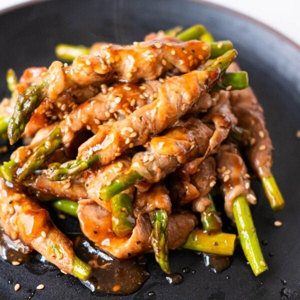 Pork wrapped asparagus with black pepper sauce glazed and white sesame on top.